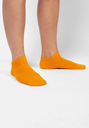 Orange ankelstrømper lavet af et glat, strækbart materiale. Har en ribbet kant og sømløs tå, der viser en ensfarvet farve uden mønstre.