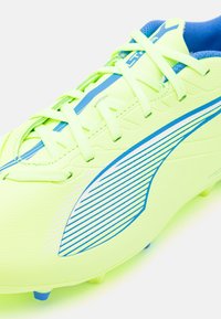 Botín de fútbol amarillo neón con acentos azules, que presenta un material sintético texturizado, cordones rectos y un diseño aerodinámico con rayas horizontales.
