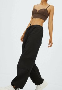 Haut court marron avec détails ajustés et fines bretelles, associé à un pantalon noir ample avec taille élastique et poches latérales. Baskets blanches.