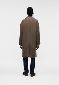 Καφέ παλτό από μαλλί με μακριά, ίσια γραμμή και φαρδύ γιακά, με απλό σχέδιο στην πλάτη. Συνδυάζεται με σκούρο τζιν και καφέ παπούτσια.