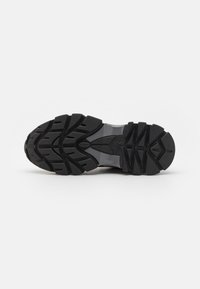 Semelle de chaussure de sport noire avec des reliefs profonds, une surface texturée et une section centrale en matériau transparent pour un confort supplémentaire.