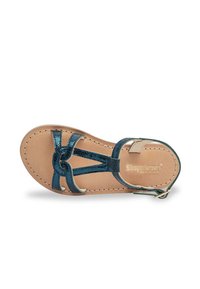 Sandalia plana con correas metálicas en color teal, plantilla de cuero y suela de color claro. Presenta un diseño de tira en T y hebilla de tobillo para el cierre.