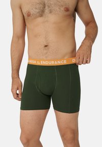 Tmavě zelené boxerky s oranžovým pasem, na kterém je vytištěno "DANISH ENDURANCE". Tkanina vypadá měkce a těsně obepíná tělo.