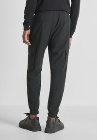 Zwarte cargobroek met een elastische tailleband, voorzien van twee zijzakken, geribbelde boorden en een glad, textuurachtig stof. Gecombineerd met zwarte sneakers.