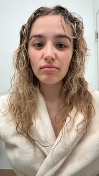 Krämfärgad morgonrock med mjuk, plyschig struktur. Lockigt hår, naturlig hudton, minimal sminkning. Bakgrunden är ljus och neutral.