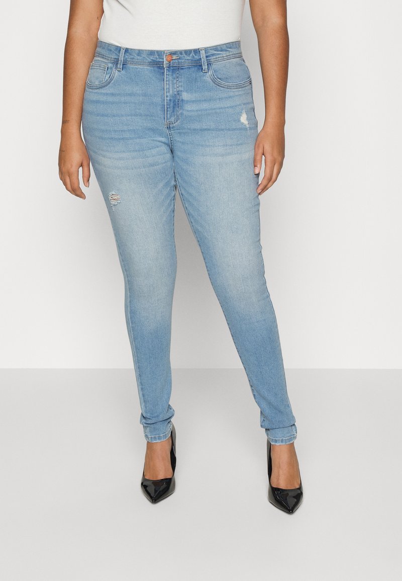 Jean skinny bleu clair en denim, avec une légère déchirure au genou gauche, cinq poches et une fermeture à bouton en laiton.