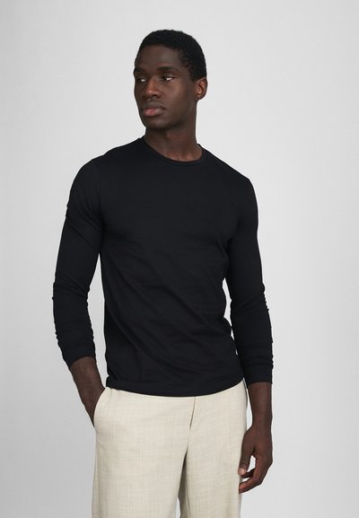 Sort langærmet skjorte fremstillet af letvægtsstof, med rund halsudskæring og tætsiddende design. Sammen med beige, strukturerede bukser.