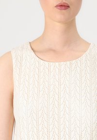 Valkoinen hihaton mekko, jossa on teksturoitu zigzag-kuvio. Materiaali on kevyen kudottu, ja siinä on sileä pinta.