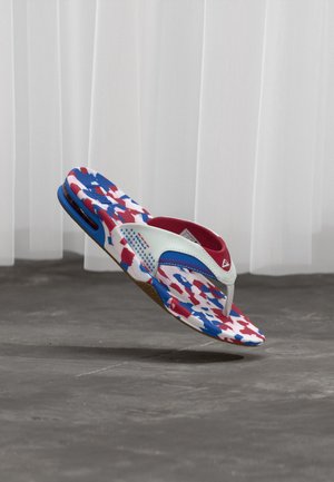 Tong multicolore rouge, blanche et bleue à motifs avec des brides blanches et bleues, montrée flottant au-dessus d'un sol carrelé gris.