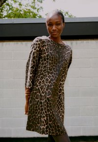 Leopardenmusterkleid mit lockerer Passform, Dreiviertelärmeln und Bootsausschnitt. Weicher Stoff mit glatter Textur und erdigen Farbtönen.