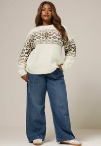 Cremfarbener Pullover mit braunen geometrischen Mustern, kombiniert mit lockeren blauen Jeans. Weicher Stoff, lässige Passform und weite Beine.