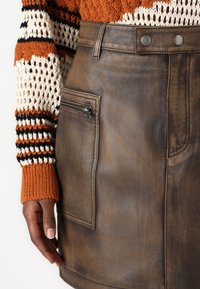 Gonna in pelle marrone con tasca con zip laterale, abbinata a un maglione a maglia texture con righe arancioni, crema e nere.