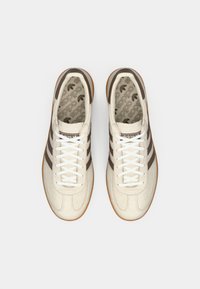 Scarpe sportive bianche con strisce marroni, in materiale scamosciato, punta tonda, lacci bianchi e suola in gomma. La fodera presenta un motivo a logo ripetuto.