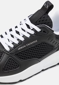 Black leather and mesh sneaker with white laces, featuring "ARMANI EXCHANGE" logo and textured accents. Sole is predominantly white.