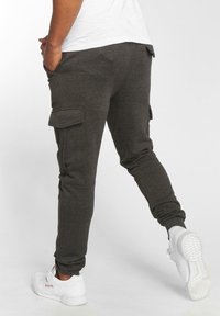 Ciemnoszare dresy z bocznymi kieszeniami typu cargo, slim fit, ściągacze na końcach nogawek i miękka tekstura, w komplecie z białymi butami sportowymi.