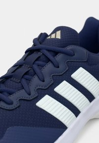 Chaussures de sport bleues avec une tige en tissu texturé, trois bandes blanches et un col rembourré. Elles disposent d'une fermeture à lacets et d'une semelle en caoutchouc.