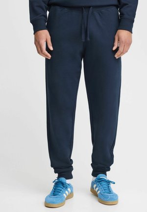 Marine joggebukser laget av myk tekstil, med elastisk midje med snøring og avsmalnede mansjetter, kombinert med blå joggesko.