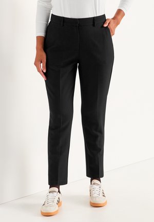Zwarte op maat gemaakte broek met een slim fit, voorzien van voorzakken en een gladde textuur. Gecombineerd met witte sneakers met oranje accenten.