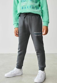 Grå sweatpants med elastisk midja och dragsko, med tryckta textdetaljer. Matchas med vita sportskor.