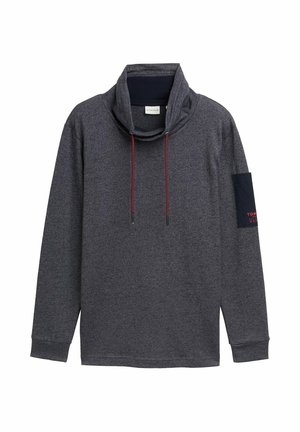 Hedvábný šedý pulovr s dlouhým rukávem a vysokým výstřihem, se stahovacími šňůrkami a námořnickou nášivkou na levém rukávu s červeným textem. Vyrobeno z měkké, texturované tkaniny.