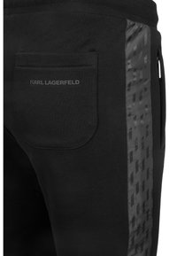 Sorte sweatpants med en baglomme, der har et subtilt "KARL LAGERFELD" logo, og et sidelæder med et struktureret sort mønster.