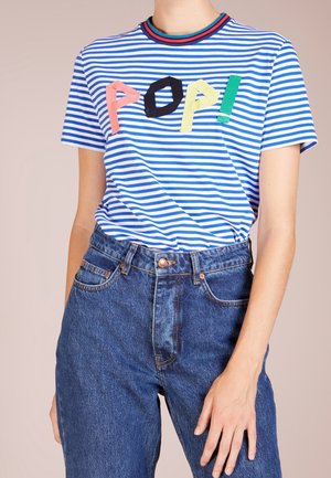 Person wearing a blue and white striped shirt with colorful "POP!" letters and high-waisted blue denim jeans, standing with one hand down.