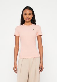 Jasnoróżowy prążkowany t-shirt z krótkimi rękawami i okrągłym dekoltem. Posiada małe zielone logo na lewej piersi. Wykonany z rozciągliwej bawełnianej mieszanki tkanin.