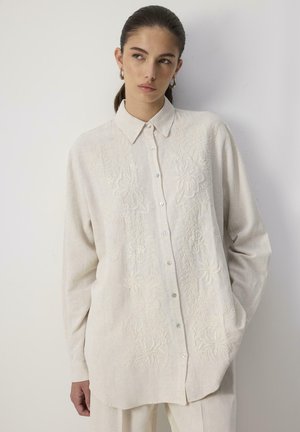Cream-colored button-up shirt with floral embroidery, long sleeves, and a structured collar, made from lightweight fabric.