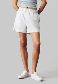 Shorts de rayas verde claro con cintura elástica y detalle de botón. Confeccionados en tejido suave. Presentan aperturas laterales para mayor comodidad.