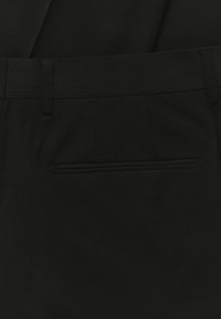 Black tailored trousers made of textured fabric, featuring a flat front, belt loops, and a discreet rear pocket with a horizontal opening.