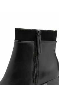 Stivale corto nero realizzato in pelle e camoscio, con zip laterale, texture liscia e tacco basso a blocco.
