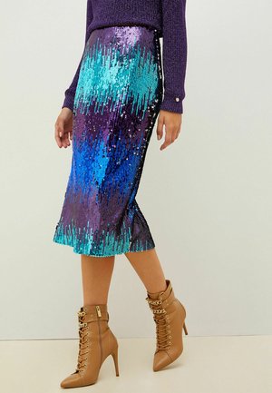 Mujer con falda midi de lentejuelas azul y morada, suéter morado y botines marrones con cordones, tacón alto y detalle de cadena dorada.