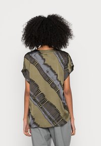 Kortärmad skjorta i olivgrön med svarta och grå abstrakta ränder. Mjuk tygkvalitet, avslappnad passform och rundad nederdel.