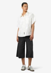Camicia bianca a maniche corte con tessuto testurizzato e colletto, abbinata a pantaloni corti in denim larghi neri e scarpe da ginnastica grigio-bianco.