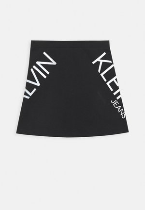 Sort bomuld mini nederdel med lige snit, elastisk talje og store hvide "KLEIN" og "JEANS" tekstaccents på hver side.