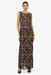 Abito da sera in pizzo nero con motivi floreali, silhouette aderente, scollatura rotonda e orlo fluido. Indossato con tacchi neri a punta.