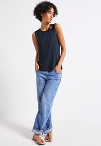 Top scollato senza maniche di colore scuro con scollatura rotonda e aperture laterali, abbinato a jeans di denim azzurro chiaro e sandali beige. Design semplice e alla moda, con una vestibilità morbida.
