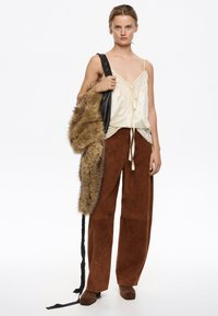Crèmekleurige satijnen camisole met kantafwerking, bruine suède broek met wijde pijpen en een bruine nep-bont tas met een zwarte schouderband. Gecombineerd en gelaagd ontwerp.