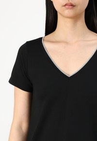 Black short-sleeve t-shirt with a V-neck featuring a silver trim along the neckline. Soft texture, simple design.