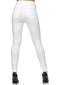 Jeans ajustados blancos con una textura suave, cinturilla alta y dos bolsillos traseros. Combinados con zapatos de tacón alto negros.