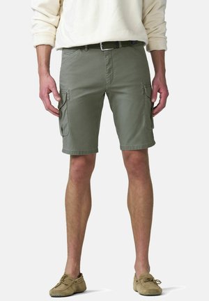 Homme portant un pull beige, un short cargo vert olive avec des poches latérales, une ceinture noire et des mocassins marron clair, debout sur un fond blanc.