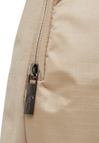 Beżowa torba z tkaniny z teksturowanym wykończeniem, gładkim zamkiem błyskawicznym i metalowym uchwytem zamka z wygrawerowanym logo.