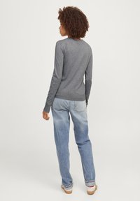 Grauer Langarmpullover mit geripptem Saum, getragen mit hellblauen, lässig geschnittenen Jeans. Glatte Textur, schlichtes Design und keine sichtbaren Muster.