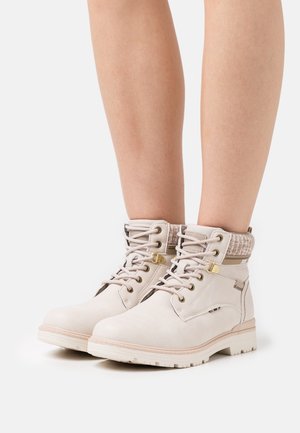 Beżowe botki za kostkę z fakturowanym kołnierzem, okrągłym noskiem, metalowymi oczkami i sznurowanym zapięciem. Gumowa podeszwa z bieżnikiem dla lepszej przyczepności.