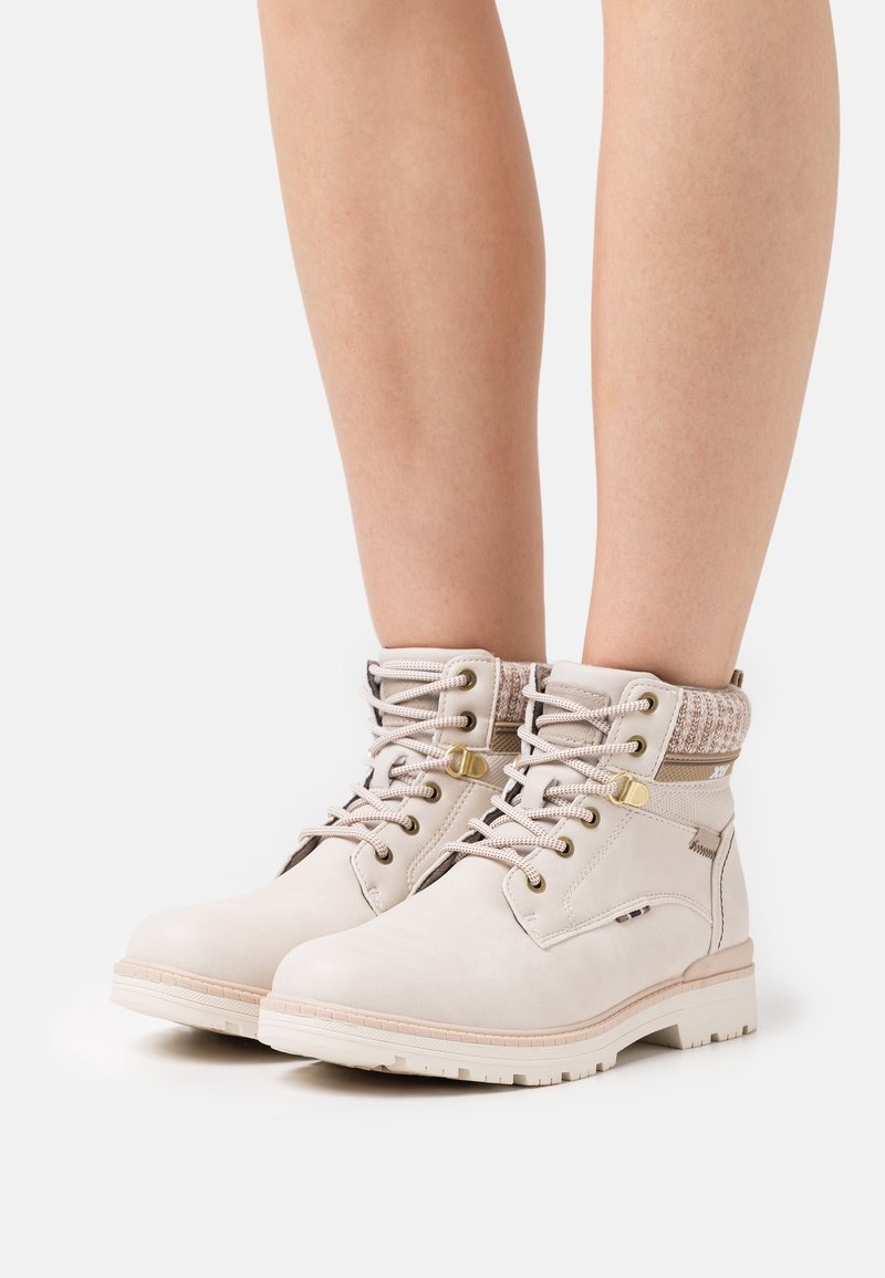 Bottes de cheville beiges avec col en tissu texturé, bout rond, œillets en métal et design à lacets. Semelle en caoutchouc avec motif pour une bonne adhérence.