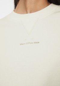 Felpa color crema con colletto rotondo, tessuto morbido e dettagli cuciti discreti, con logo "Marc O’Polo DENIM" stampato in chiaro.
