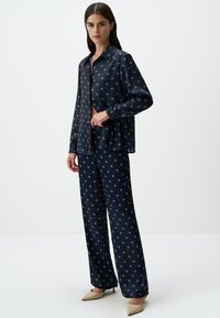 Navy satijnen pyjama set bestaande uit een overhemd met lange mouwen en een kraaghalslijn, en bijpassende wijde broek, beiden versierd met kleine witte patronen.