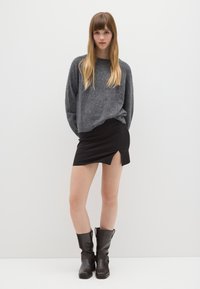 Pull gris à motifs, mini-jupe noire avec une fente sur le côté, et bottines en cuir marron avec des sangles. Tenue simple et décontractée.