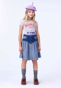 Světlofialový baret, tričko s nápisem "Human Kind" v barevných písmech, džínová sukně s rozšířeným střihem, šedé podkolenky, hnědé boty.