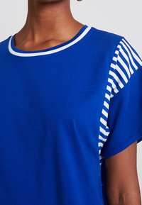 Blue cotton T-shirt featuring a solid color front and striped sleeve design, with a rounded white collar and short sleeves. Soft texture.